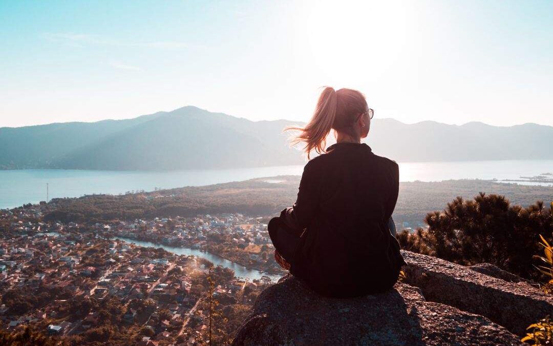 A visually striking image featuring a confident woman sitting in serene nature at sunrise, symbolizing success and purpose. She gazes out at the horizon with an expression of peace and focus.